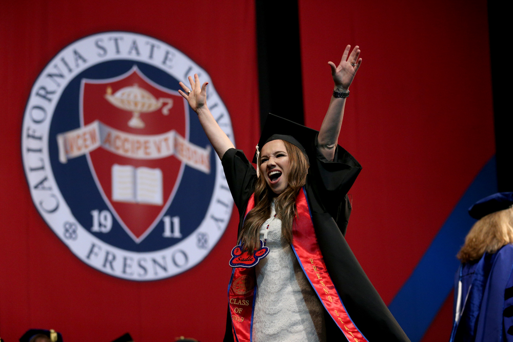 Graduate walking across the ceremony stage with her hands in the air.