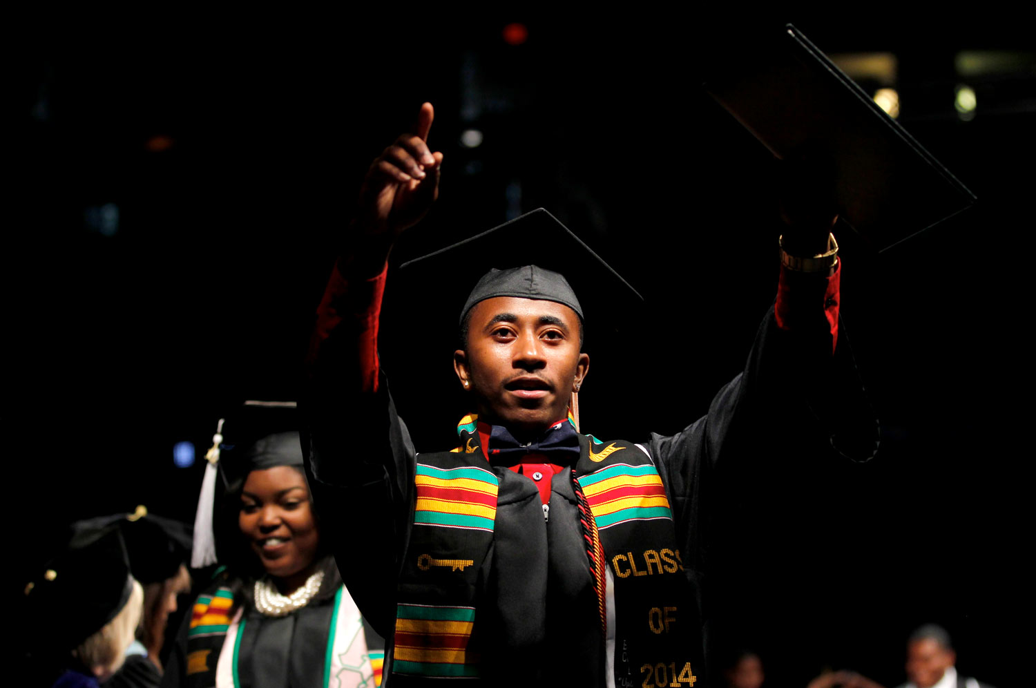 Graduating student in regalia pointing to the audience